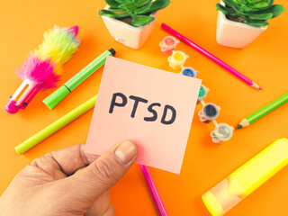 PTSD acronym Post Traumatic Stress Disorder handwritten on sticky note with child supplies. Mental health disorder concept