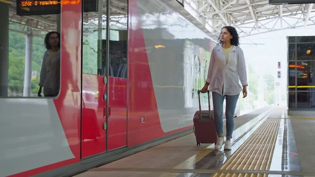 female passenger with suitcase is walking on empty platform of modern railway station suburban train
