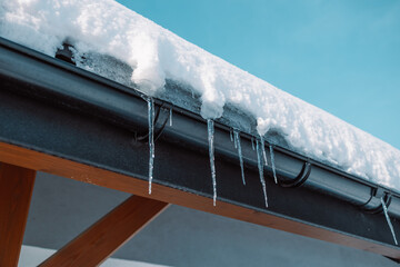Icicles hang from the roof of a log house near which a car is carelessly parked, which can be...