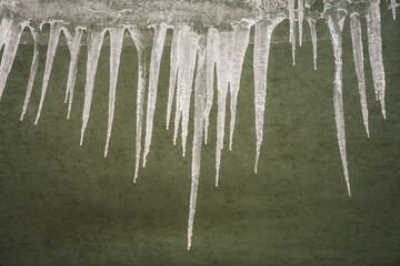 Icicles hanging from the roof on plaster wall background. Natural icicles of different sizes