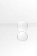 Fototapeta na wymiar Glass ball on a mirrored surface and white background.