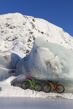 Fatbikes, 907 fat tire bike and Fatback fat tire bike, resting against giant iceberg in winter on Portage Lake, Chugach National Forest; Portage, Alaska, United States of America