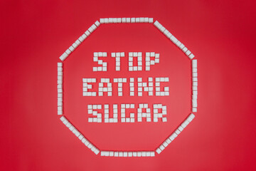 stop eating sugat text in octagonal stop sign shape frame made from sugar cubes. giving up sugar flat lay concept image isolated on red background