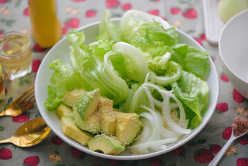Healthy salad plate,low calories,Avocados sprinkled with white sesame seeds, green leafy vegetables, onions, Salad dressing ingredients is olive oil,natural vinegar, mustard,Clean healthy eating food.