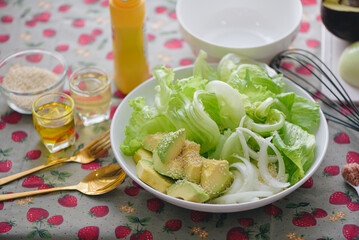 Healthy salad plate,low calories,Avocados sprinkled with white sesame seeds, green leafy vegetables, onions, Salad dressing ingredients is olive oil,natural vinegar, mustard,Clean healthy eating food.