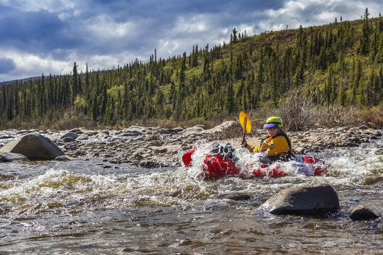 Woman packrafter negotiating a tributary of the Charley River in summertime, splashing through the last of a rapid, Yukon&ndash;Charley Rivers National Preserve; Alaska, United States of America