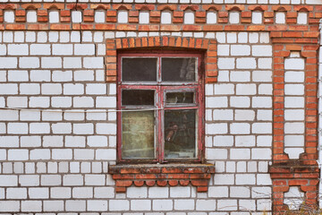 Fototapeta na wymiar Old wooden window with a red frame in a white and red brick house.