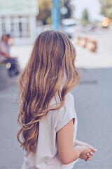 Stylish woman girl with beautiful hair walking outdoors in summer city street. View from back