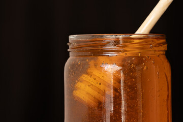 A jar of honey on a black background. wooden spoon for honeyHoney jar with dipper on the black background, macro shot.