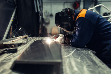 The worker makes spot welding of metal parts in the factory, sparks, and glow