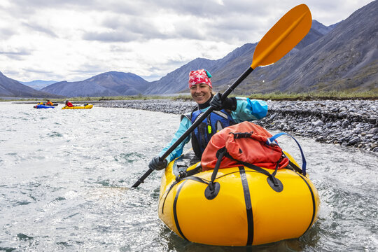 Woman smiling and paddling packraft boat on the Marsh Fork River, Brooks Range, ANWR, Alaska, USA