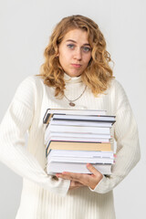 Attractive young curly female student holding a stack of books and wondering