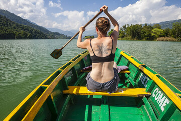Caucasian woman paddling boat on the green colored Fewa Lake near Pokhara on a hot sunny day; Kaski District, Nepal