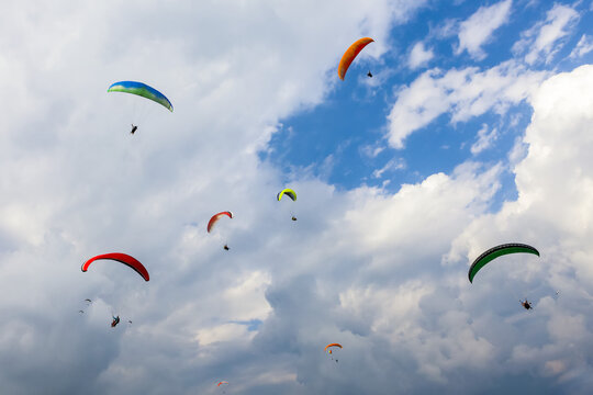 A group of colorful paragliders playing in the thermals above Sarangkot and the city of Pokhara on a sunny autumn day with a cloudy sky; ‎Kaski District, Nepal