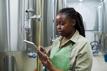 Black young woman referring to tablet computer when checking fermentation process - obrazy, fototapety, plakaty
