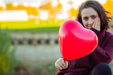 Mujer de raza caucásica mostrando el globo rojo con forma de corazón que le ha regalado su pareja por San Valentín en una cita romántica.