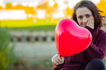 Mujer de raza caucásica mostrando el globo rojo con forma de corazón que le ha regalado su pareja...