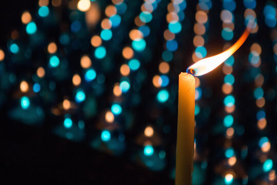 A candle with flame in front of rows of other candles.; Chartres, France