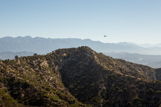 A helicopter flies over the hills outside of Los Angeles and Hollywood near Griffith Observatory.; Griffith Observatory, Los Angeles, California