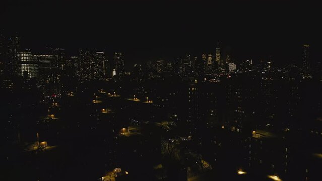 Forwards fly above night metropolis. Multistorey apartment buildings in urban borough and downtown skyscrapers in background. New York City, USA