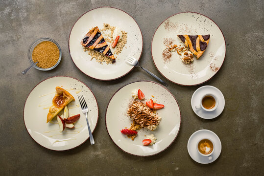 View from directly above of a variety of cakes on plates with forks and cappuccinos; Studio