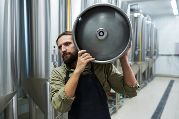 Microbrewery owner carrying keg with drink to warehouse