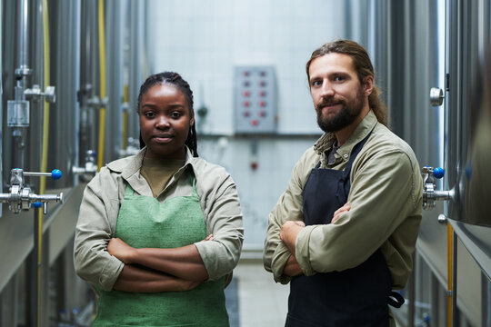 Smiling team of microbrewery workers standing with arms crossed