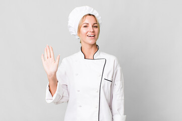 caucasian blonde woman smiling happily, waving hand, welcoming and greeting you. chef concept © kues1