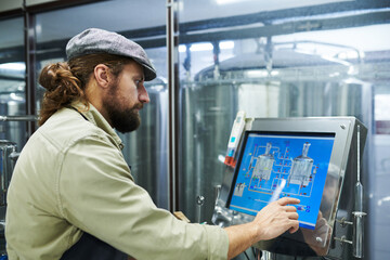 Naklejka na ściany i meble Brewery worker checking scheme on screen when setting brewery equipment