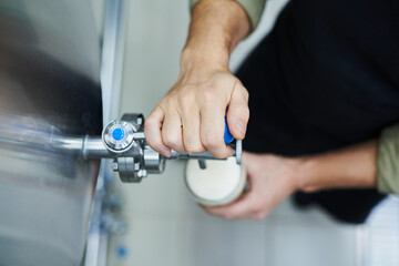 Close-up image of brewery worker pouring beer from tank in big glass
