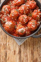 Italian meatballs with parmesan in spicy tomato sauce close-up in a frying pan on the table. Vertical top view from above