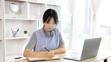 Asian woman taking notes in notebook while studying online in laptop at home, Video chat, Online communication , Stay home, New normal, Distance learning.., Social distancing, Learn online...