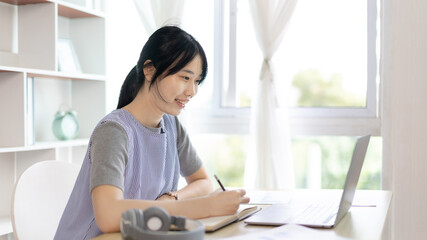 Asian woman taking notes in notebook while studying online in laptop at home, Video chat, Online communication , Stay home, New normal, Distance learning.., Social distancing, Learn online...