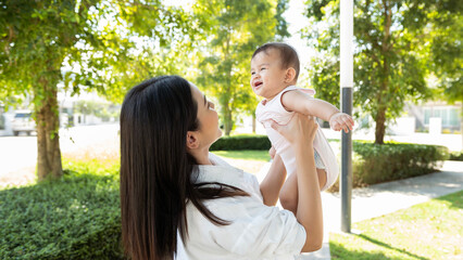 Fototapeta premium Beautiful mom holding a baby girl in her arms outdoor in sunshine day.