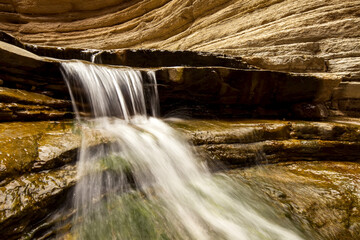 A waterfall flows over layers of desert rock.