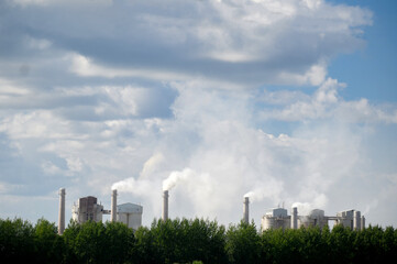 Fototapeta na wymiar Tall chimneys of a factory with smoke rising up, polluting the atmosphere. Air pollution concept.
