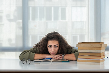 Young college woman law student frustrated with pile of books she need to read and study for exam....