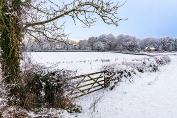 Dusk falling on early winter snow on the lodge and gates to Miserden Park near the Cotswold village of Winstone, Gloucestershire, England UK