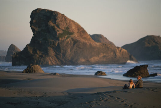 Two people converse on the rocky beach at twilight.; Pistol River, Oregon.