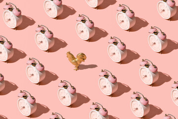 Vintage alarm clock and golden rooster figurine, creative pattern against pastel pink background. Minimal creative concept. Wake up on time in the morning.  