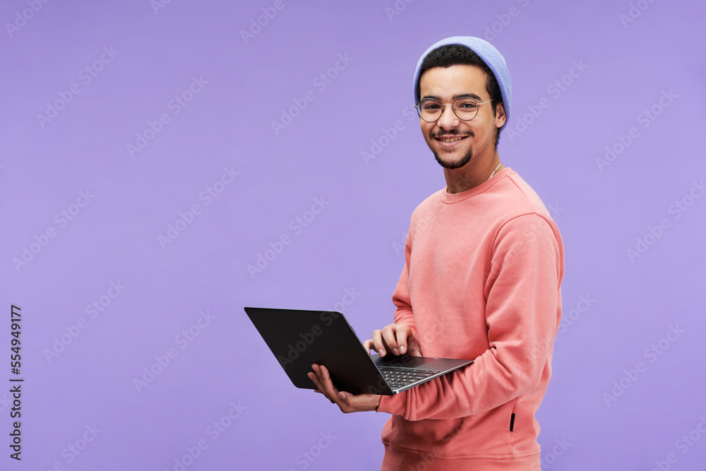 Poster young successful designer or freelancer in casualwear using laptop and looking at camera with smile 