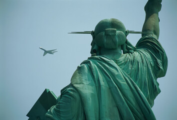 An airplane flies near the Statue of Liberty in a bright blue sky on a sunny day; New York City, New York, United States of America