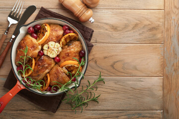 Baked chicken thighs with orange, cranberry and spicy herbs rosemary servered in frying pan on light wooden rustic background. Festive Christmas Dinner Concept menu. Top view. copy space