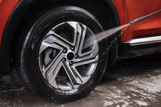 Washing red luxury car in detailing service. Close up image of the process of washing the car wheels rims with a high pressure water gun after cleaning .