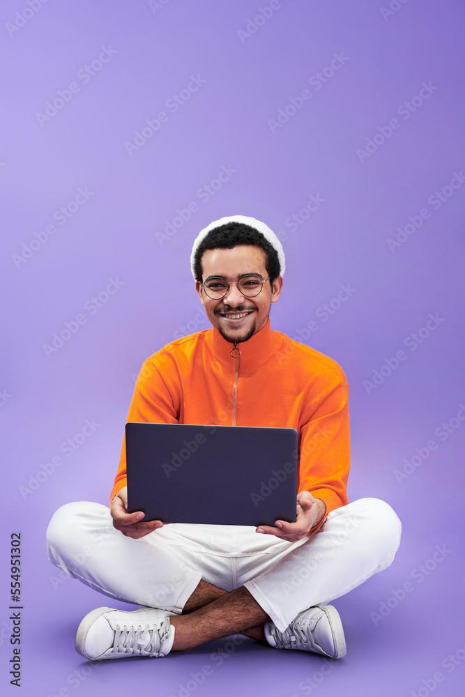 Aufkleber Successful young male designer or programmer using laptop and looking at camera while sitting on the floor with his legs crossed
