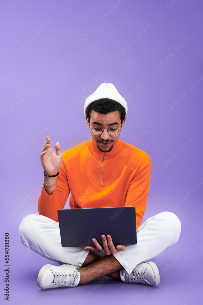 Aufkleber Young man looking at laptop screen with astonishment while sitting in front of camera with his legs crossed and networking