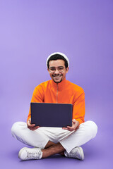 Successful young male designer or programmer using laptop and looking at camera while sitting on...