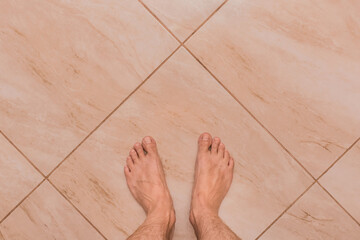 Barefoot men's feet stand on the light ceramic tile floor background, view from above