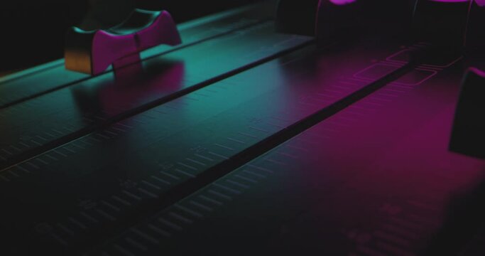 Close-Up Finger pushes audio mixer fader to max volume in colorful party lights