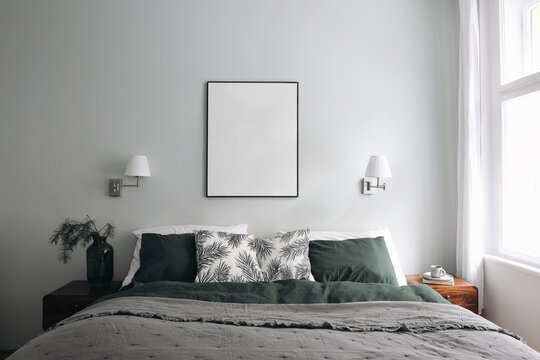Vertical black picture frame mockup on sage wall. Elegant bedroom view. White, green linen pillows, blanket. Night stand with pine tree branches, vase and cup of coffee. Christmas winter interior.